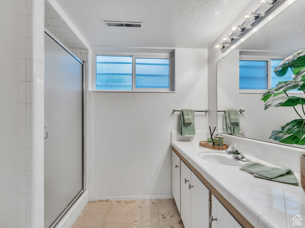 Bathroom featuring a shower stall, vanity, a textured ceiling, baseboards, and tile patterned floors