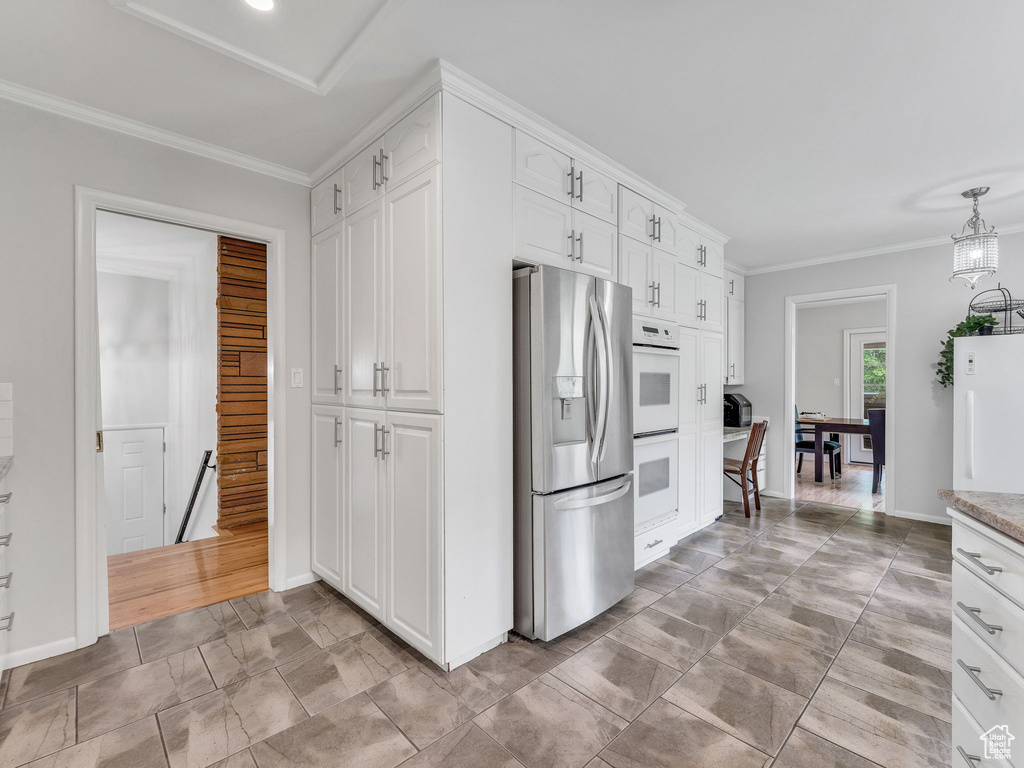 Kitchen with white appliances, white cabinetry, crown molding, baseboards, and light stone countertops