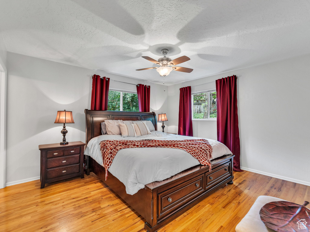 Bedroom with multiple windows, light wood-style flooring, baseboards, and a textured ceiling