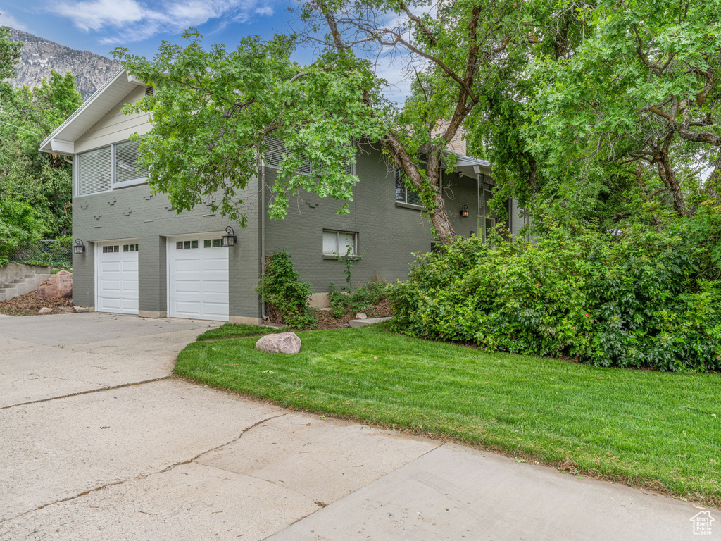 View of side of home featuring driveway, brick siding, a lawn, and a garage