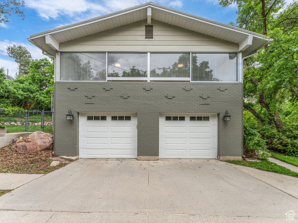 View of front of house with an attached garage, fence, driveway, and brick siding