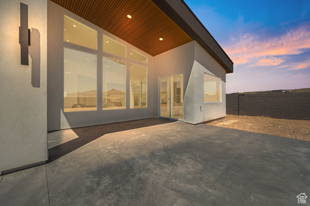 Back of house at dusk featuring fence, a patio, and stucco siding
