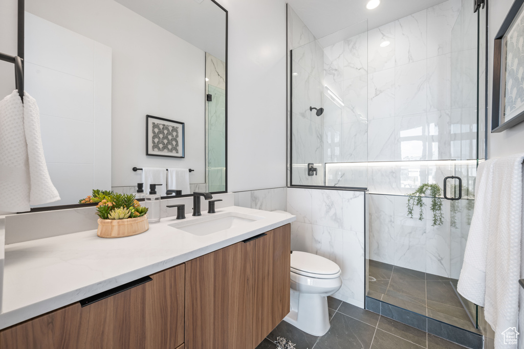Full bathroom with a marble finish shower, toilet, vanity, tile walls, and recessed lighting
