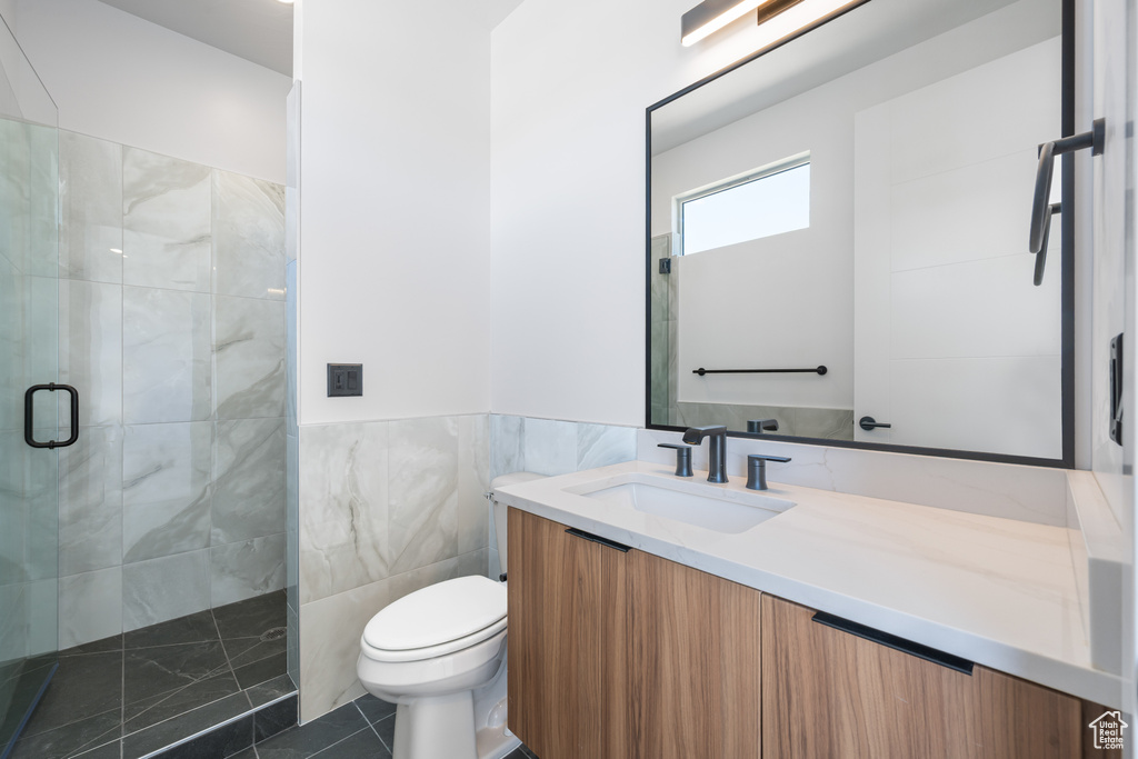 Bathroom with a stall shower, toilet, vanity, tile patterned flooring, and tile walls