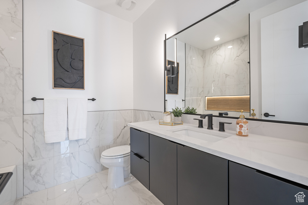 Bathroom with tile walls, marble finish flooring, toilet, vanity, and a wainscoted wall