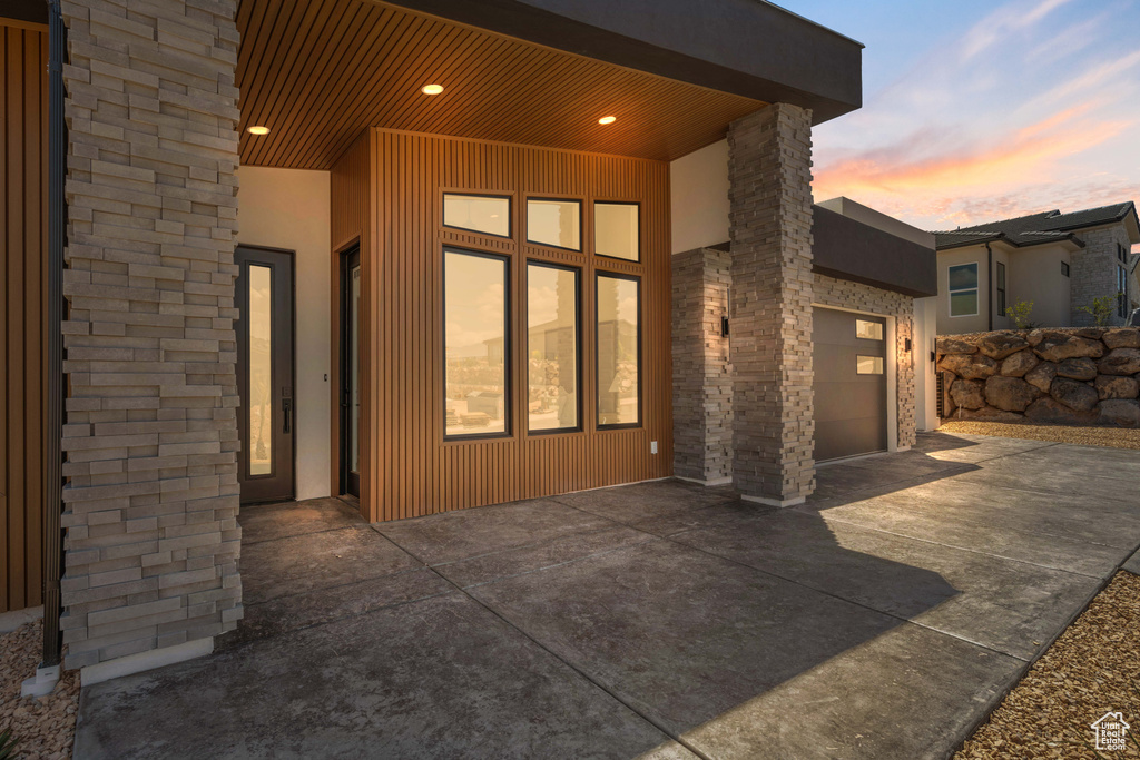 Rear view of house featuring driveway, an attached garage, stone siding, and stucco siding