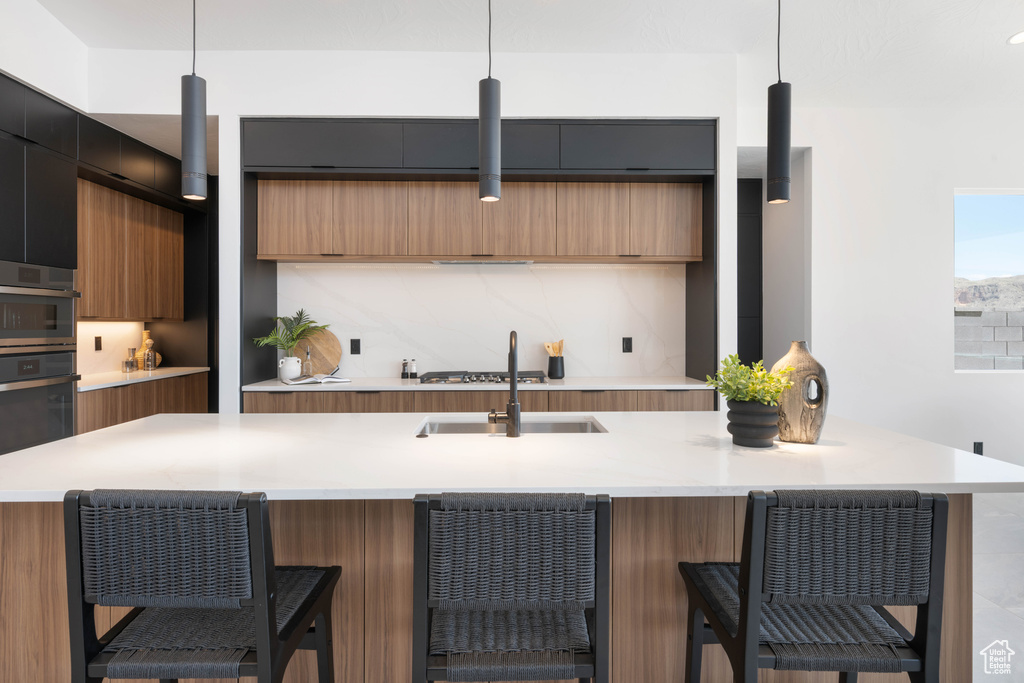 Kitchen with modern cabinets, a sink, light countertops, decorative backsplash, and brown cabinets