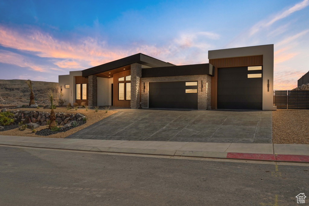 Contemporary house with a garage, concrete driveway, stone siding, and stucco siding