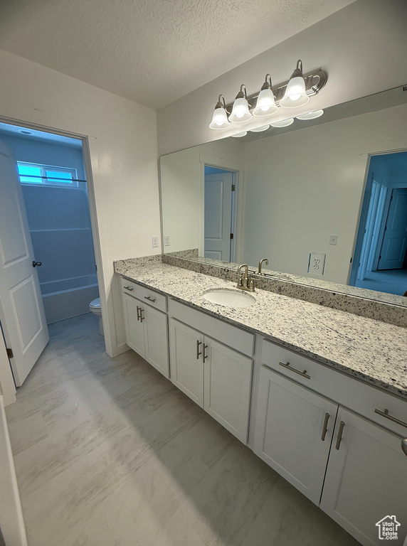 Bathroom with vanity, toilet, a textured ceiling, and a bath