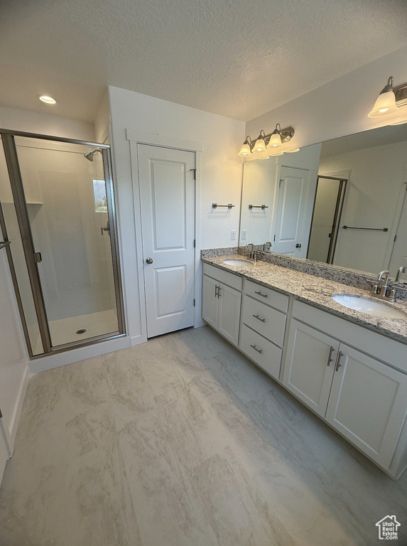 Bathroom featuring a shower stall, double vanity, a textured ceiling, and marble finish floors