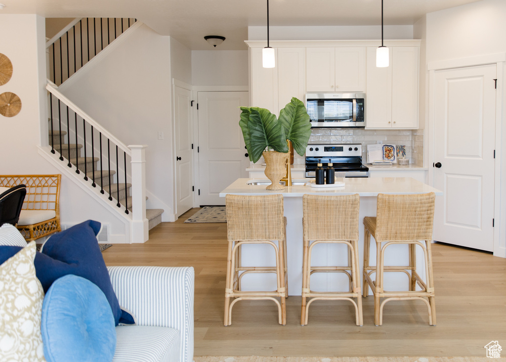 Kitchen with stainless steel appliances, light wood-type flooring, tasteful backsplash, a kitchen island, and light countertops