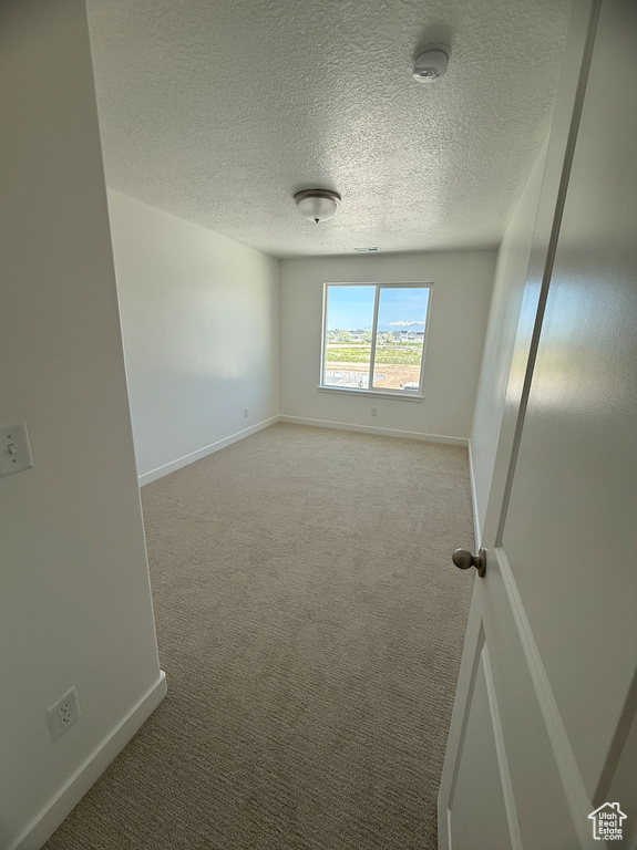 Carpeted empty room with a smoke detector, baseboards, and a textured ceiling