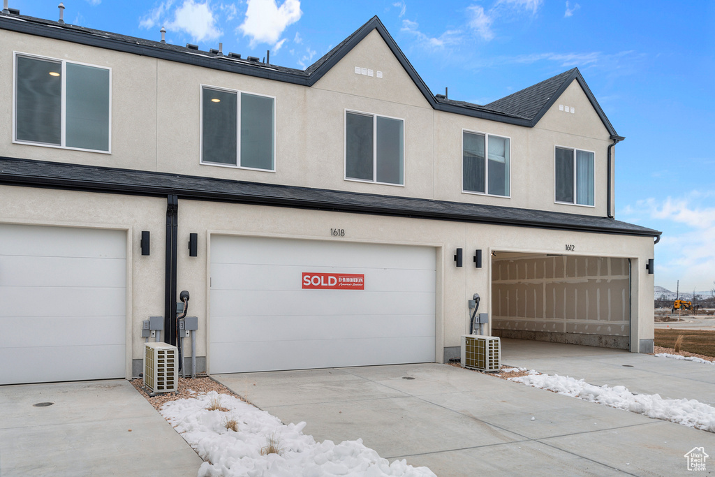 View of front of house with stucco siding, a garage, central AC, and concrete driveway