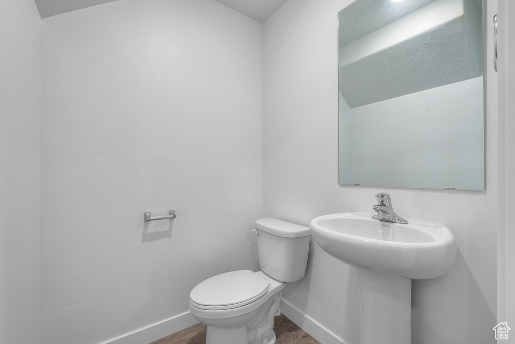 Half bath with wood finished floors, toilet, baseboards, and a sink