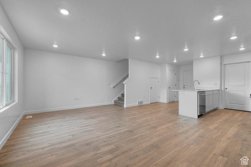 Unfurnished living room featuring recessed lighting, light wood-type flooring, stairway, baseboards, and a sink