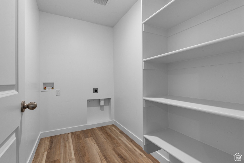 Laundry area with electric dryer hookup, hookup for a washing machine, wood finished floors, and baseboards