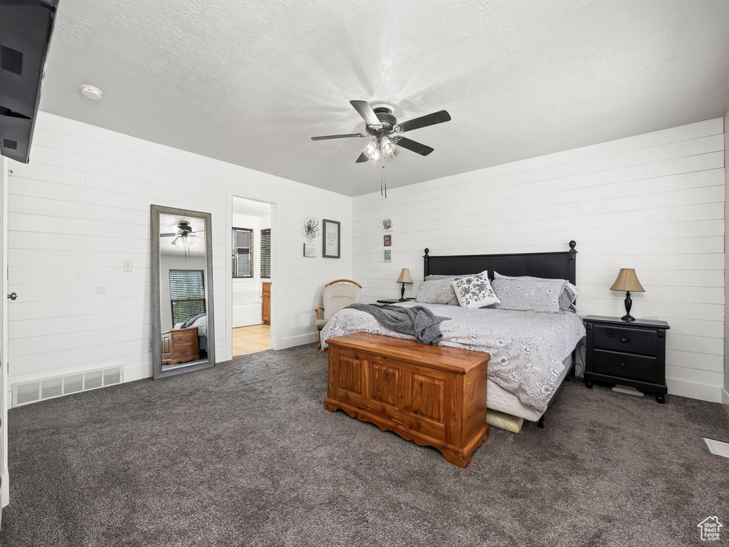 Carpeted bedroom with a textured ceiling, connected bathroom, wood walls, and ceiling fan