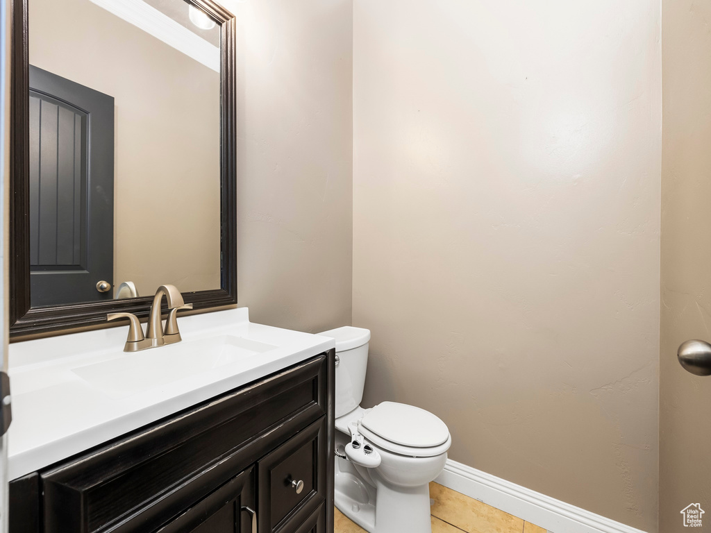 Half bath featuring toilet, tile patterned floors, vanity, and baseboards