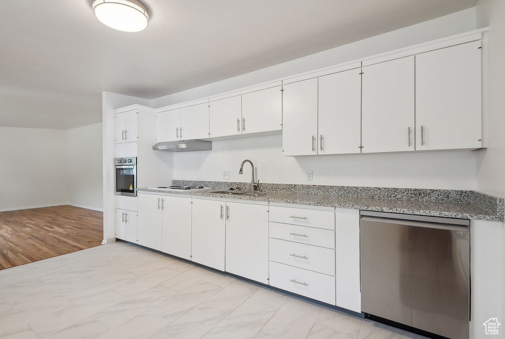 Kitchen featuring stainless steel appliances, under cabinet range hood, a sink, and white cabinetry