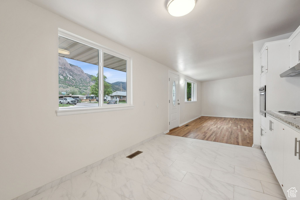 Kitchen with white cabinets, light marble finish floors, stainless steel oven, cooktop, and baseboards
