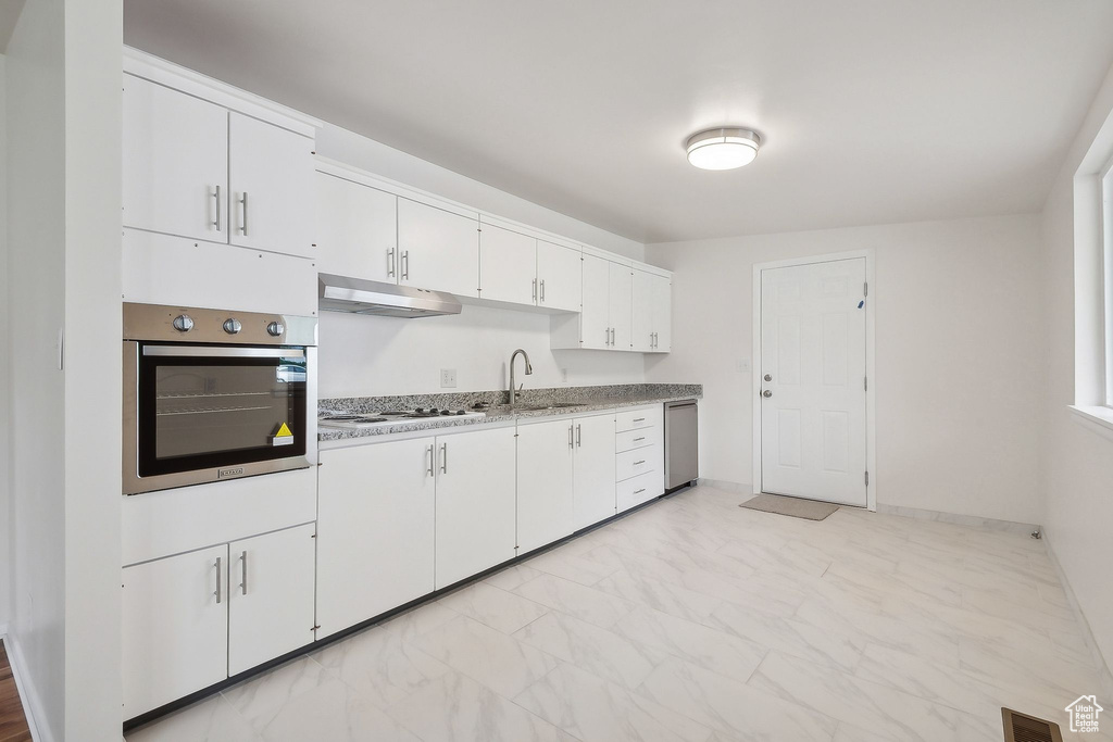 Kitchen featuring stainless steel appliances, under cabinet range hood, white cabinets, a sink, and light marble finish flooring