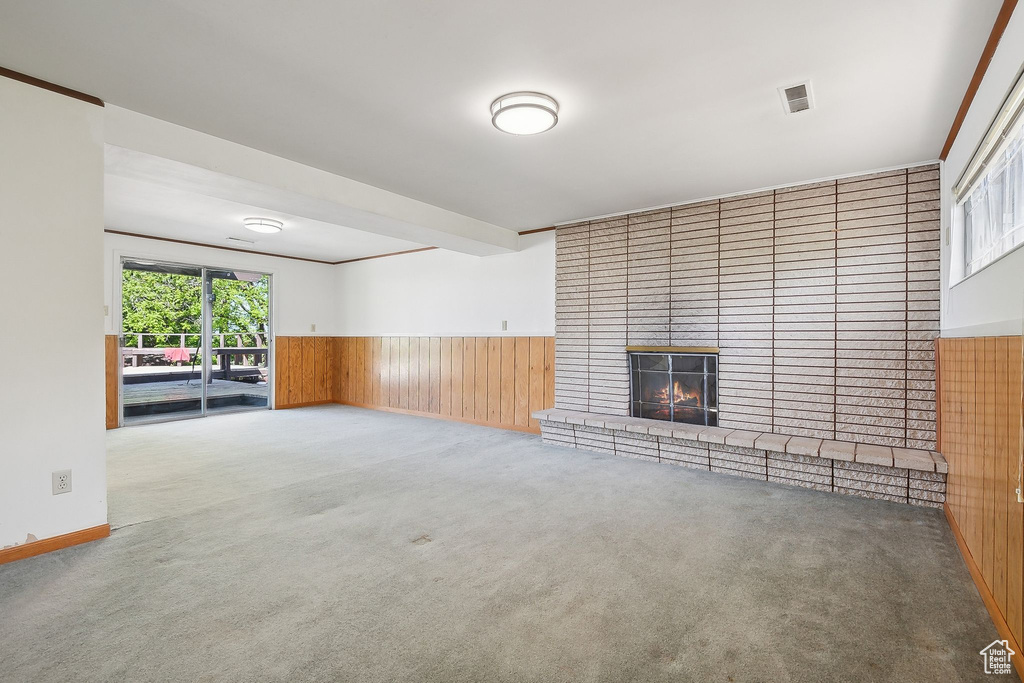 Unfurnished living room with carpet floors, a brick fireplace, wainscoting, and wood walls