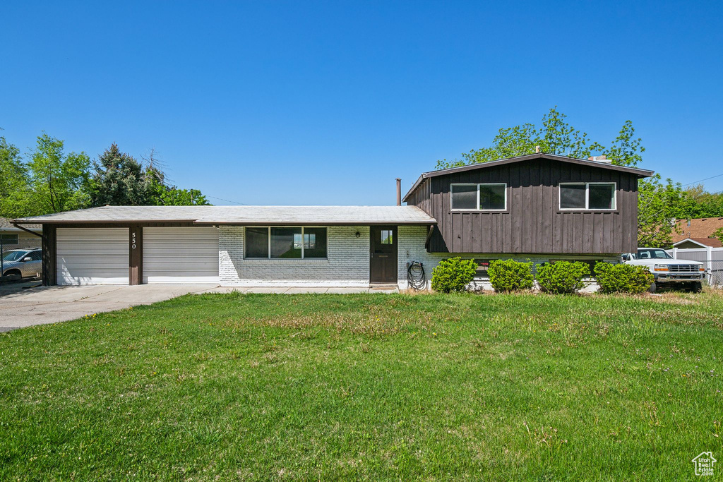 Split level home with driveway, an attached garage, a front yard, and brick siding