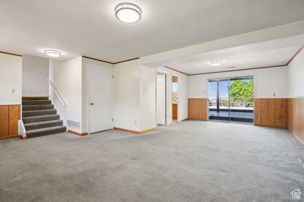 Unfurnished living room with wainscoting, stairway, carpet, wood walls, and ornamental molding