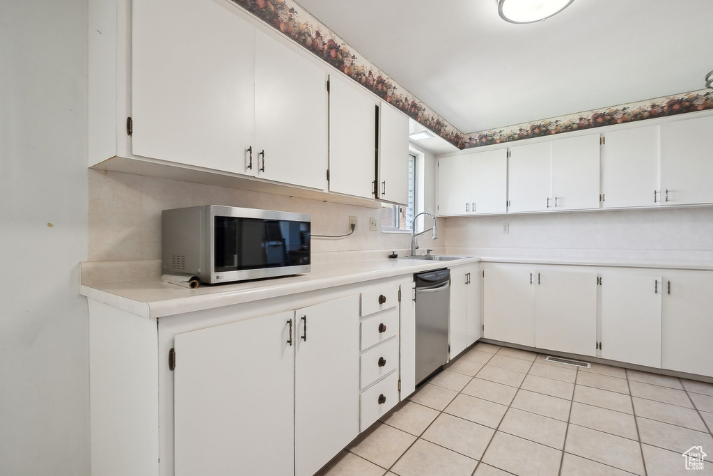 Kitchen with appliances with stainless steel finishes, a sink, light countertops, light tile patterned flooring, and white cabinetry