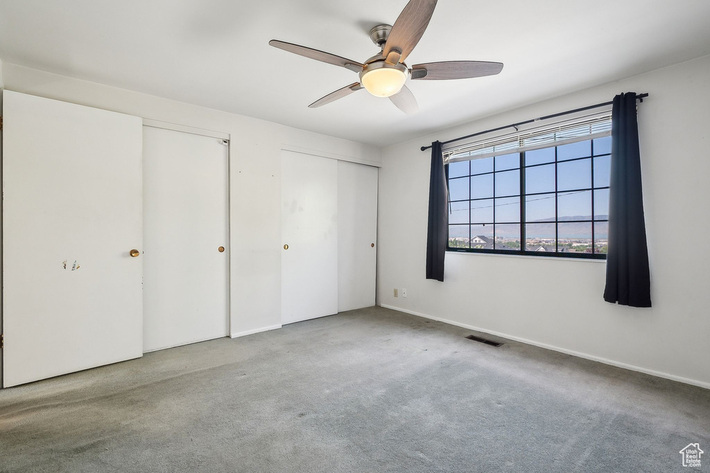 Unfurnished bedroom with carpet floors, two closets, ceiling fan, and baseboards