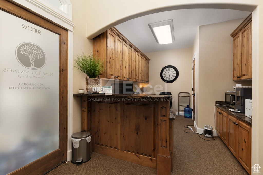 Kitchen featuring dark countertops, baseboards, carpet flooring, a peninsula, and arched walkways