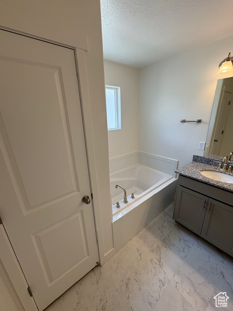 Full bath featuring vanity, marble look tile flooring, a bath, and a textured ceiling