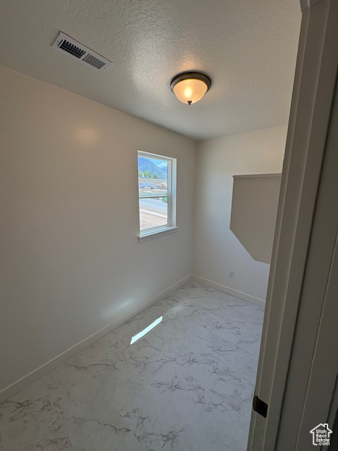 Empty room with light marble finish flooring, baseboards, and a textured ceiling