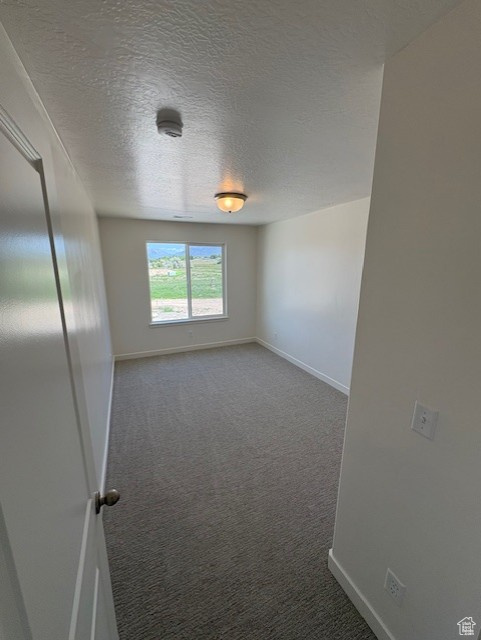 Spare room with carpet floors, baseboards, a textured ceiling, and a smoke detector