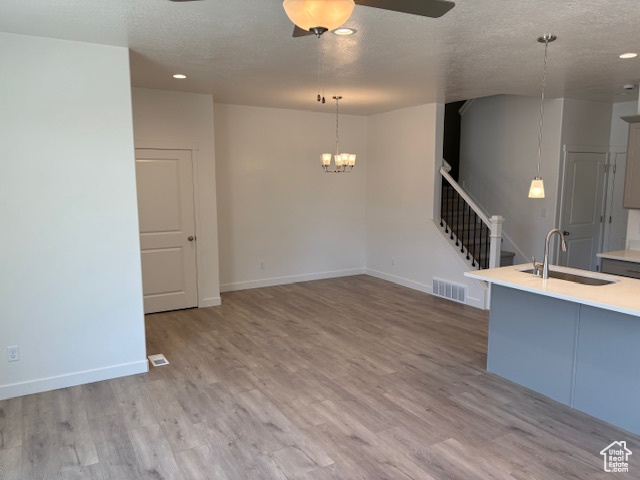 Unfurnished living room featuring a sink, a ceiling fan, wood finished floors, a chandelier, and baseboards