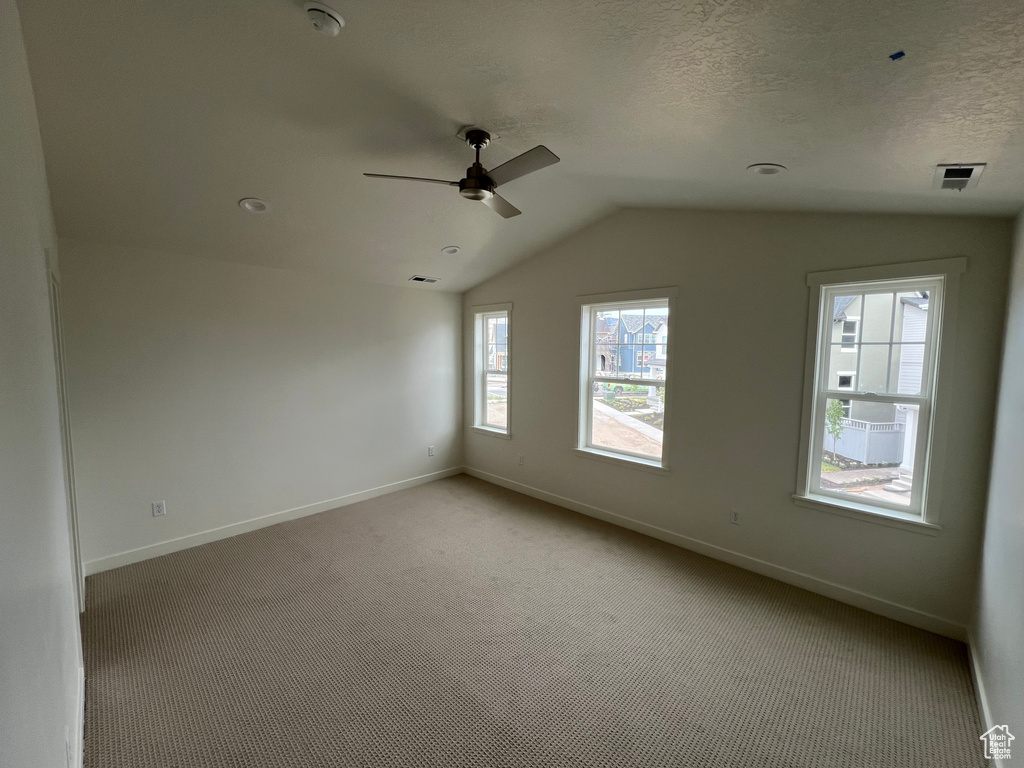 Spare room featuring lofted ceiling, ceiling fan, and light carpet