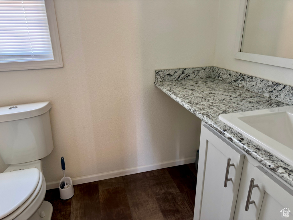Half bath with wood finished floors, vanity, baseboards, and toilet