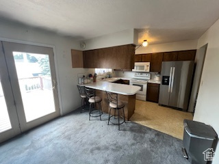 Kitchen featuring stainless steel fridge with ice dispenser, white microwave, range with electric cooktop, a peninsula, and a breakfast bar area