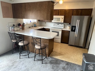 Kitchen featuring white appliances, light countertops, a breakfast bar, a peninsula, and dark brown cabinets
