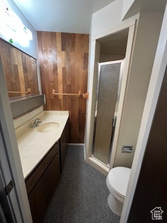 Bathroom with wooden walls, toilet, vanity, and a stall shower