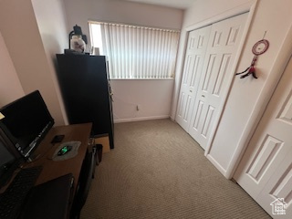 Hallway featuring light carpet, a desk, and baseboards