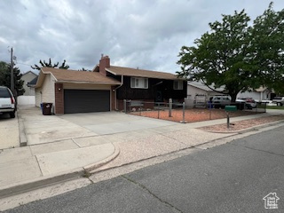View of front of property with an attached garage, concrete driveway, and fence