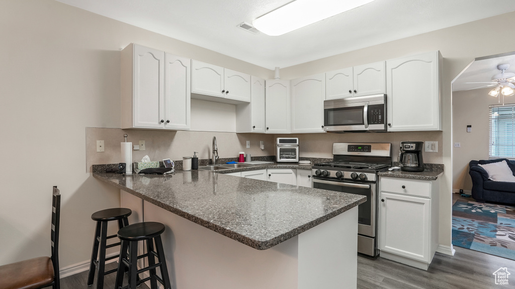 Kitchen with stainless steel appliances, a sink, a peninsula, dark wood-type flooring, and white cabinetry