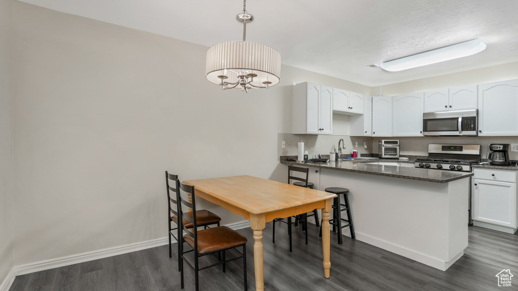 Kitchen with appliances with stainless steel finishes, dark wood-style floors, white cabinets, a peninsula, and a sink