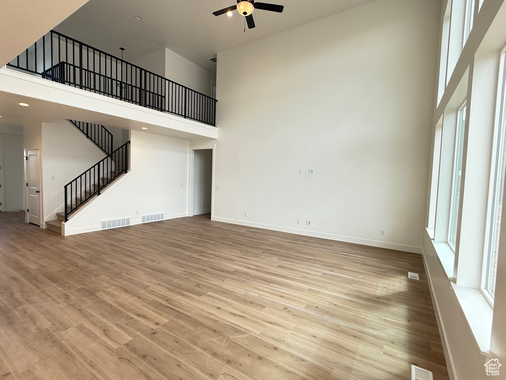 Unfurnished living room featuring plenty of natural light, a high ceiling, a ceiling fan, stairs, and light wood-style floors