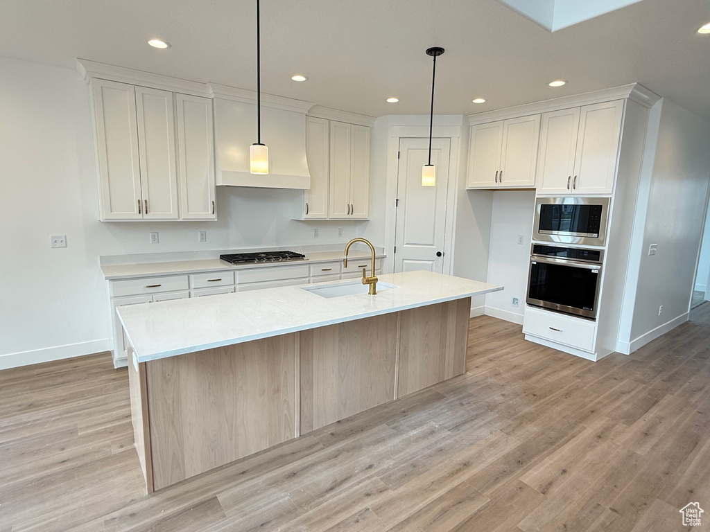 Kitchen with stainless steel appliances, a sink, baseboards, light wood-style flooring, and white cabinetry