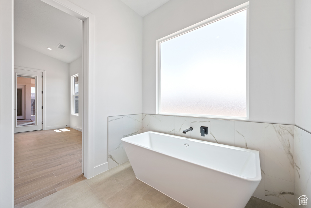 Bathroom featuring a soaking tub, tile walls, wood finished floors, and lofted ceiling