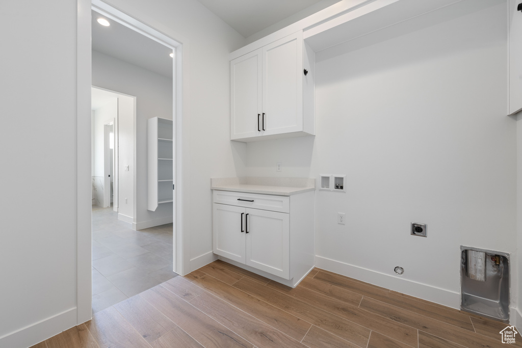 Clothes washing area featuring electric dryer hookup, hookup for a washing machine, light wood-type flooring, baseboards, and cabinet space