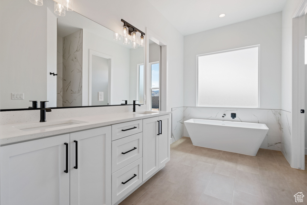 Full bathroom with a soaking tub, double vanity, tile walls, and a wainscoted wall