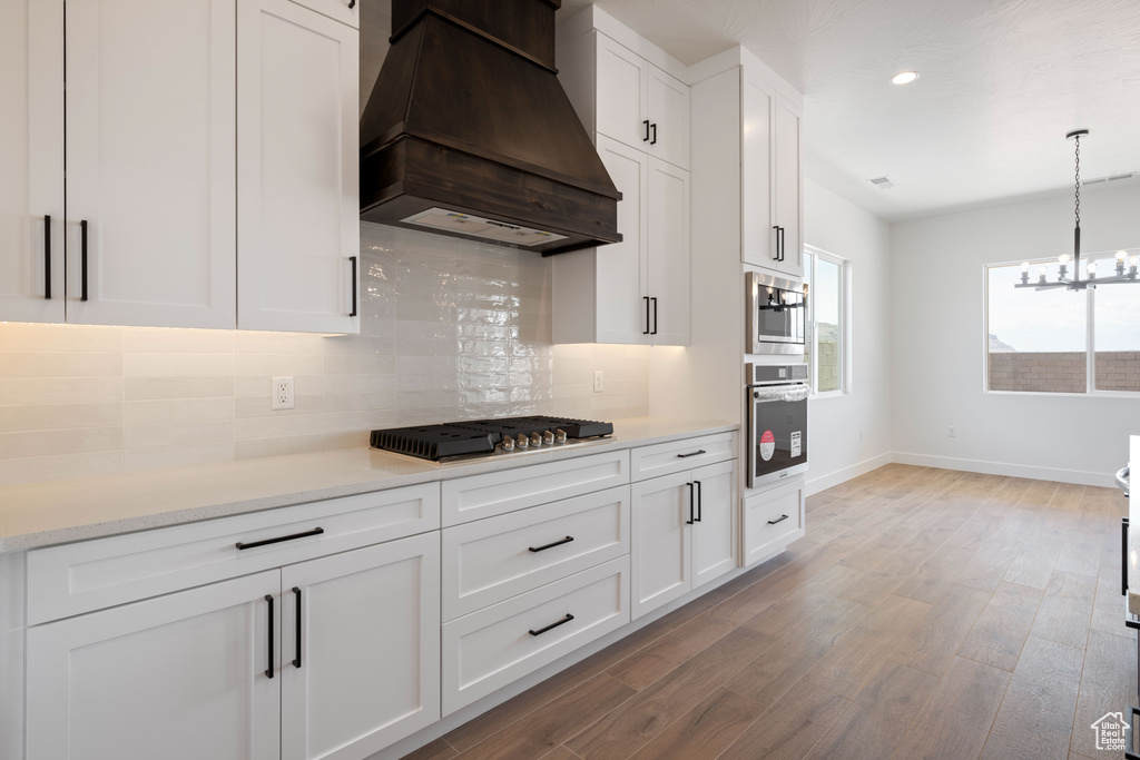 Kitchen featuring premium range hood, stainless steel appliances, decorative backsplash, baseboards, and white cabinetry